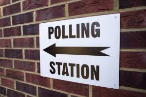 A sign on a brick wall with an arrow and the words, "polling station"
