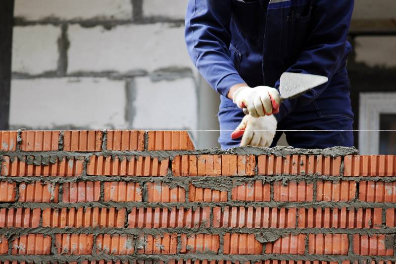 A man using a trowel and cement to build a brick wall