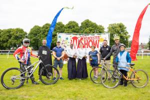 Cyclists and other performers standing in front of a Worcester Show sign